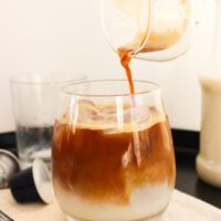 Café siendo vertido en un vaso de cristal con hielos